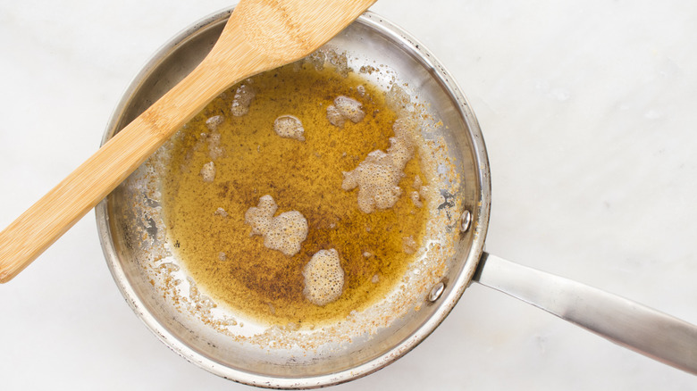 A metal skillet holding browned butter with a wooden spoon placed on top sits on a white background.
