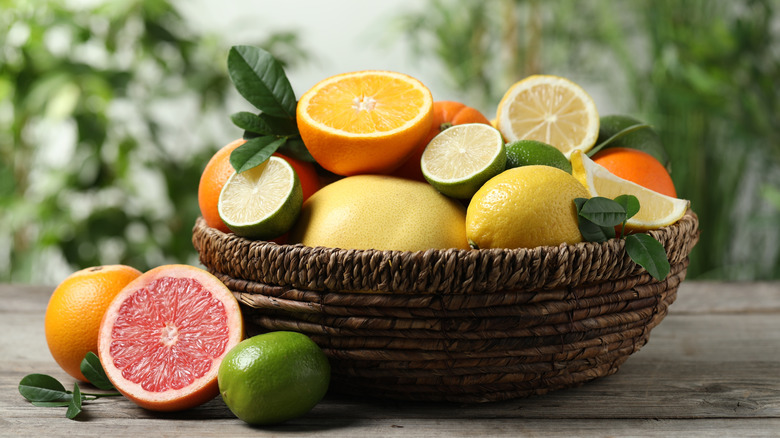 Assorted fresh citrus fruits in jute bowl on wooden table with greenery in background