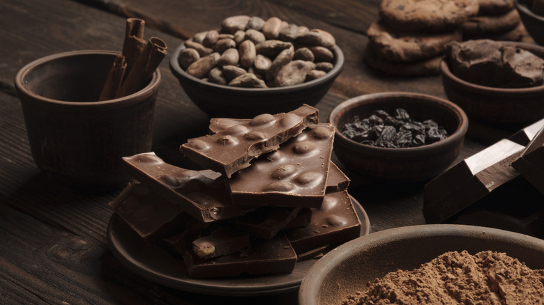 Assorted forms of chocolate are arranged in dark bowls on a wooden table.