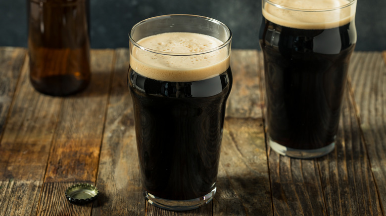 Two glasses of dark stout on a wooden table with an empty bottle in the background