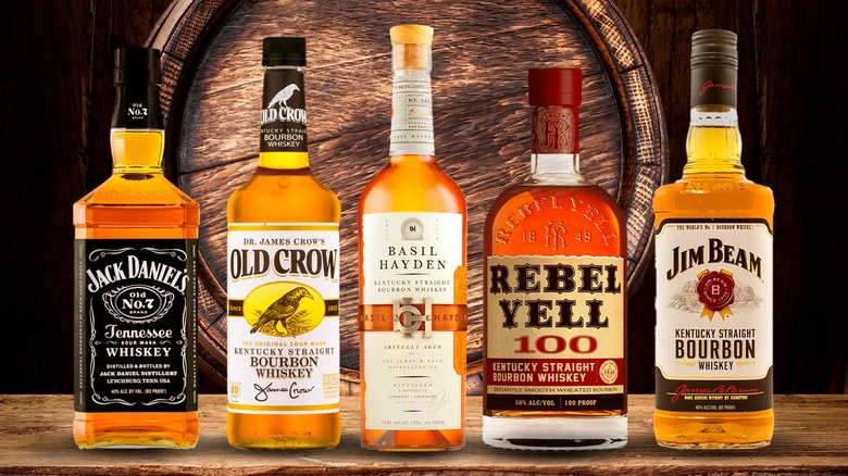 Five bottles of bourbon whiskey lined up in front of a barrel