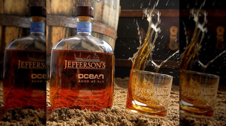 Bottle of Jefferson's Ocean Aged at Sea Bourbon on sand with glass splashing over