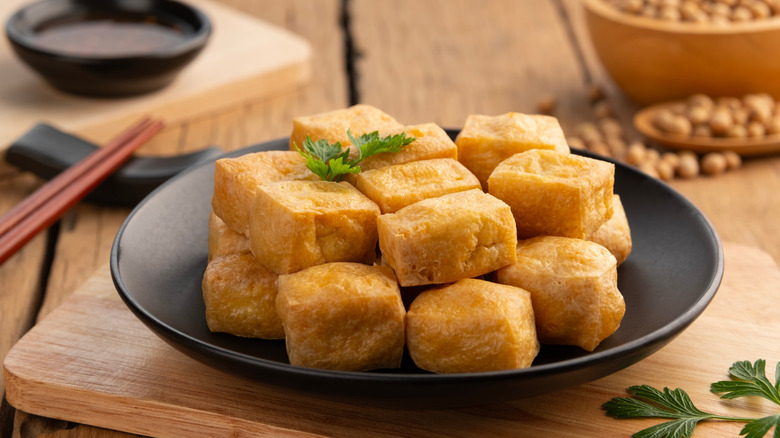 crispy tofu on black plate with chopsticks and bowl of soybeans