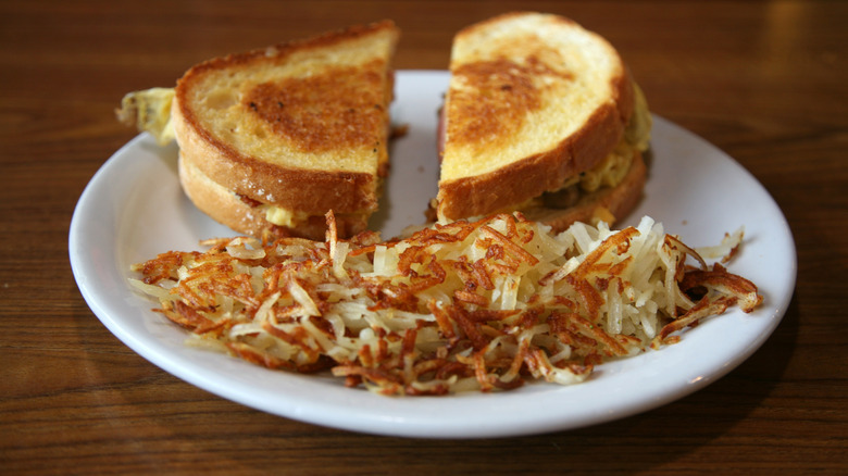 plate of hash browns next to a sandwich