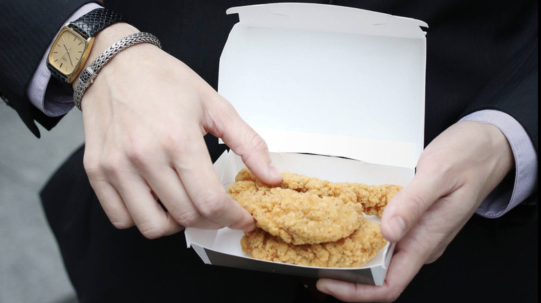 Man wearing suit and watches holds open box of Chicken Selects