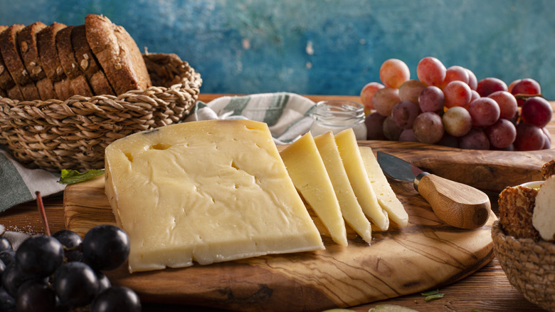 slices of Gruyère cheese on wooden cutting board with bread and fruit