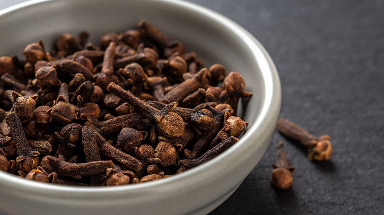 a bowl of cloves sits in a white dish on a dark surface