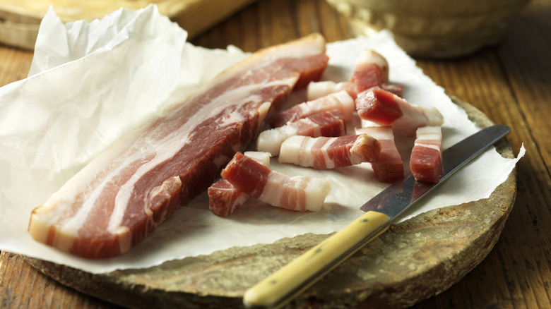 slices of cured pork belly sit beside a knife on a stone cutting board