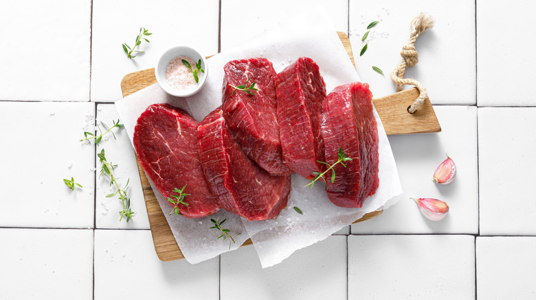 beef tenderloin sitting on cutting board against white backdrop