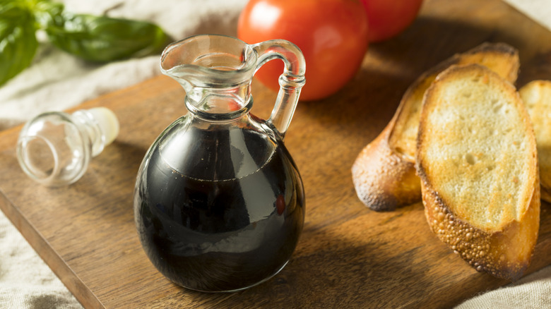 bottle of balsamic vinegar sitting beside bread and tomatoes