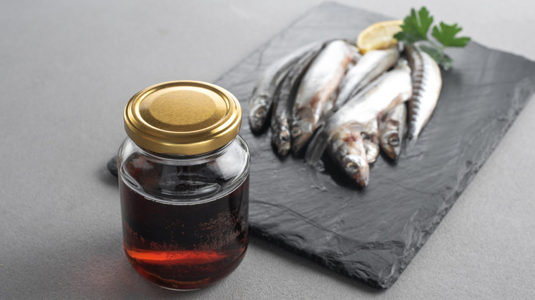 garum fish sauce sitting beside anchovies on a gray surface