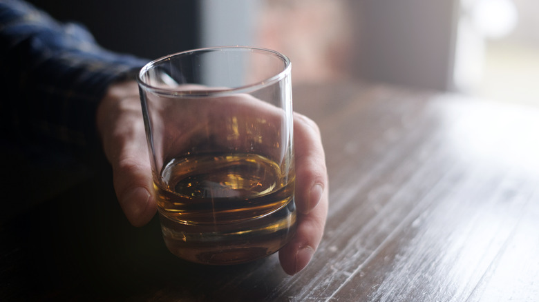 A hand holding a glass of whiskey