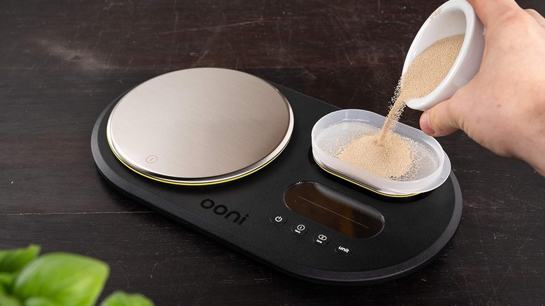A hand pouring grains onto the Ooni digital scale