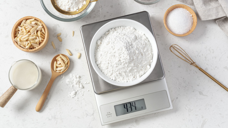 Flour in a large bown on a digital kitchen scale surrounded by scattered bowls and spoons filled with baking ingredients
