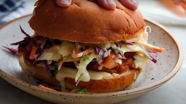 Hand pressing down on the top of a chicken and coleslaw sandwich