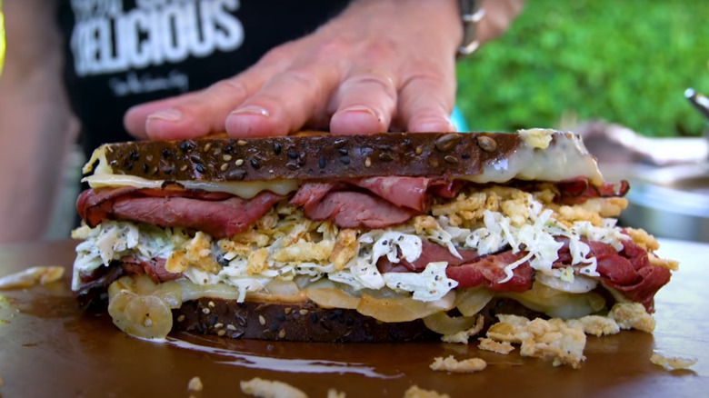 Hand pushing down on the top of a Reuben sandwich