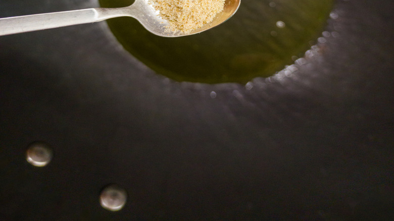 teaspoon with Asafoetida beige powder over oil in skillet