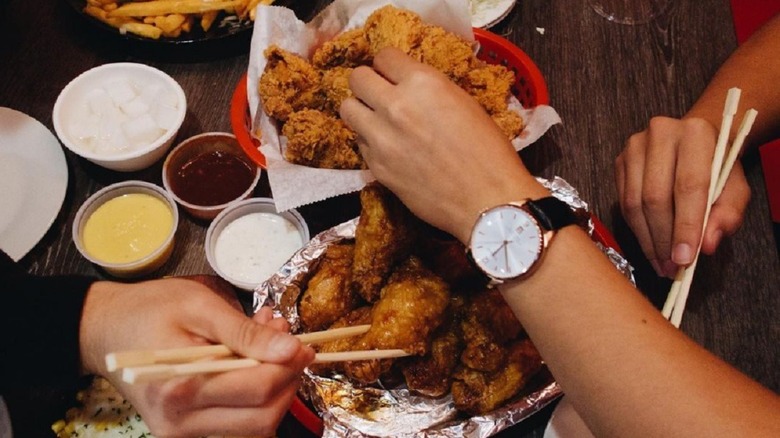 three hands grabbing fried chicken and wings