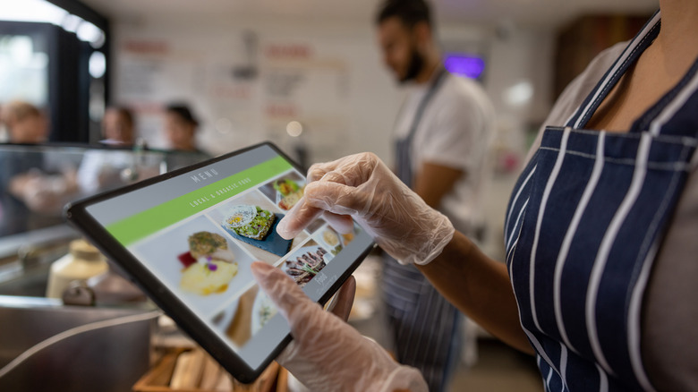 Person wearing gloves ordering food from a menu at a fast-casual restaurant