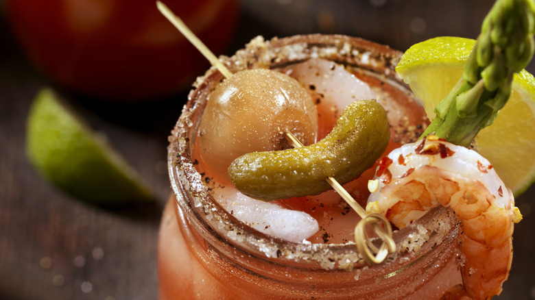 A bloody mary with a gherkin and onion on a skewer and a shrimp, asparagus, and lemon garnsih