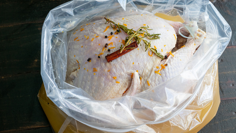 A turkey brining in a plastic bag with herbs and liquid