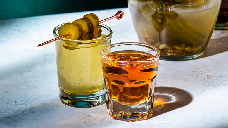 A shot of whiskey and a small glass of pickle juice with three pickles on a spear as a garnish