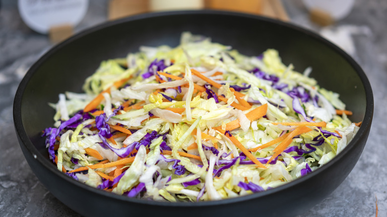 A batch of coleslaw with shredded green cabbage, red cabbage, and carrots in a black bowl