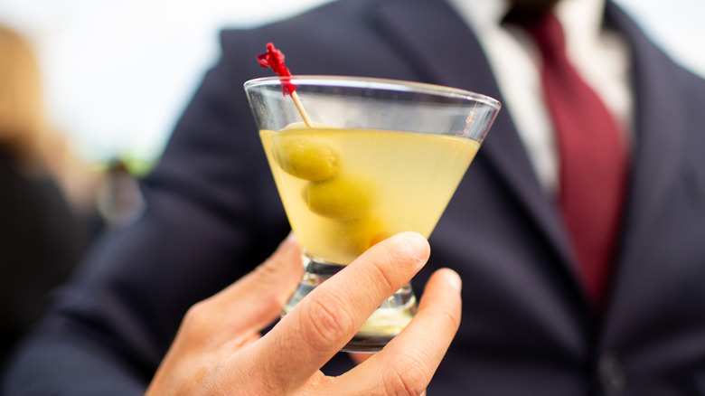 A man in a suit holds an extra dirty martini with three olives