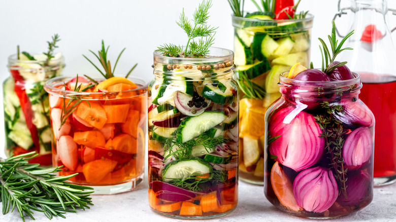 Five jars of pickled vegetables with herbs