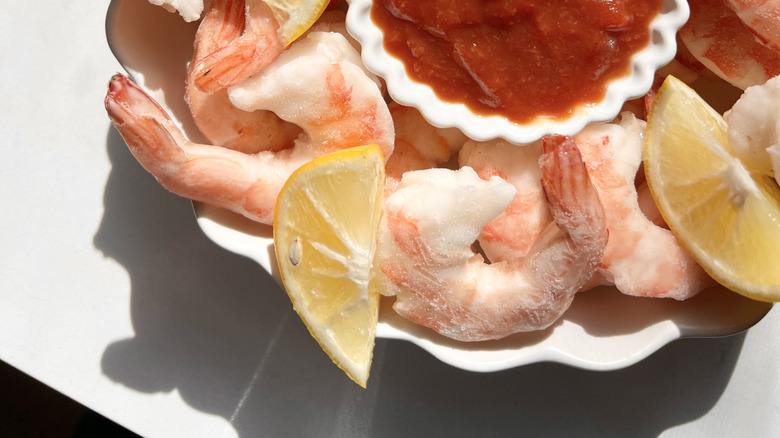 Cocktail sauce in a container on a plate filled with shrimp and lemon wedges