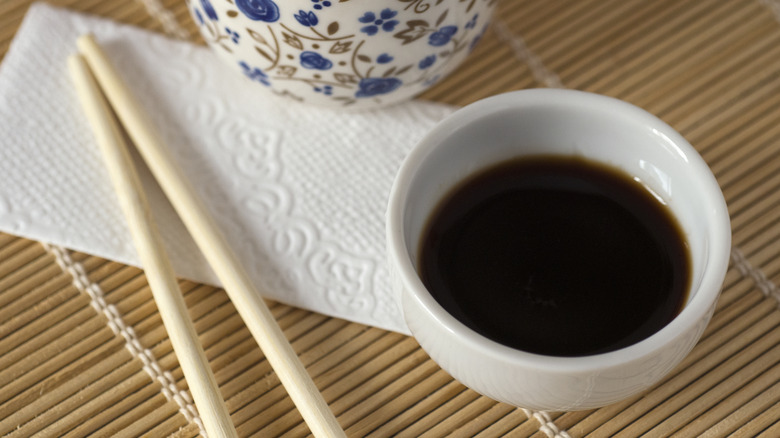 Soy sauce and chopsticks over a napkin and a bamboo placemat