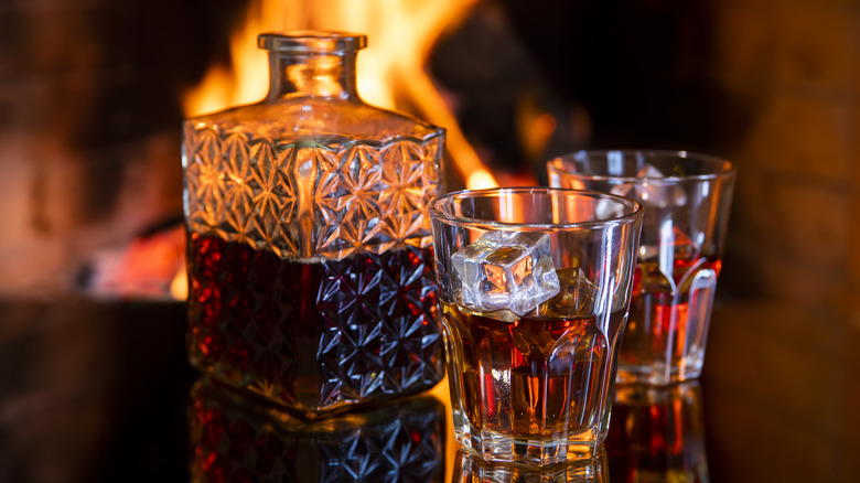 Crystal decanter of scotch and rocks glasses by a fireplace