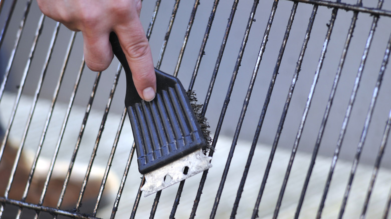 A person cleaning smoker grates with a stiff bristle grill brush