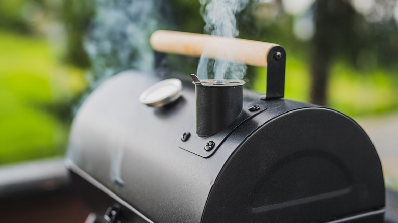 A stream of thin smoke coming out of the smokestack of a meat smoker