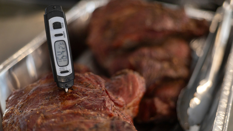 A meat thermometer inserted into a pork shoulder roast in a foil pan from the smoker