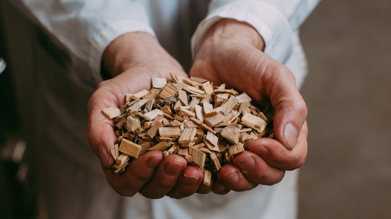 A man in a white coat holding a handful of wood chips for a smoker