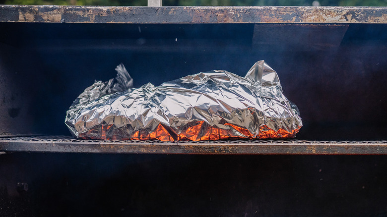 A piece of meat wrapped in foil on the grate on a meat smoker