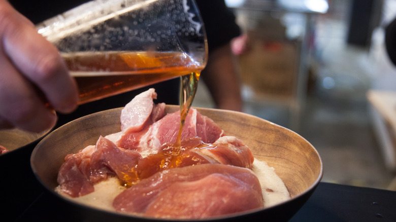 A person pouring beer onto pork