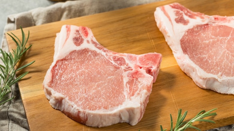 Two raw bone-in pork chops on a wooden cutting board