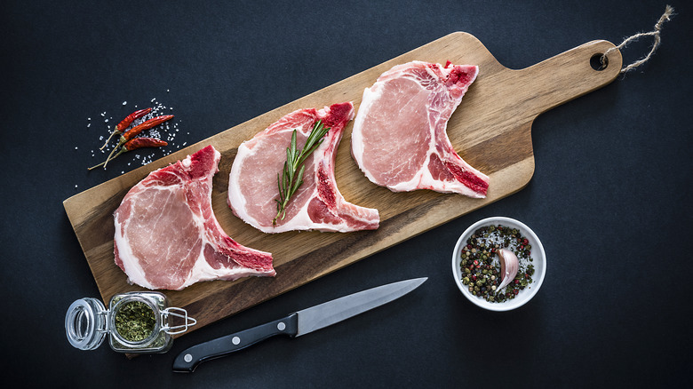 Three raw pork chops on a wooden cutting board