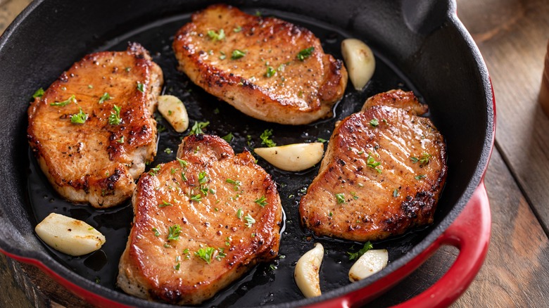 Four pork chops seared in a pan with oil and garlic cloves