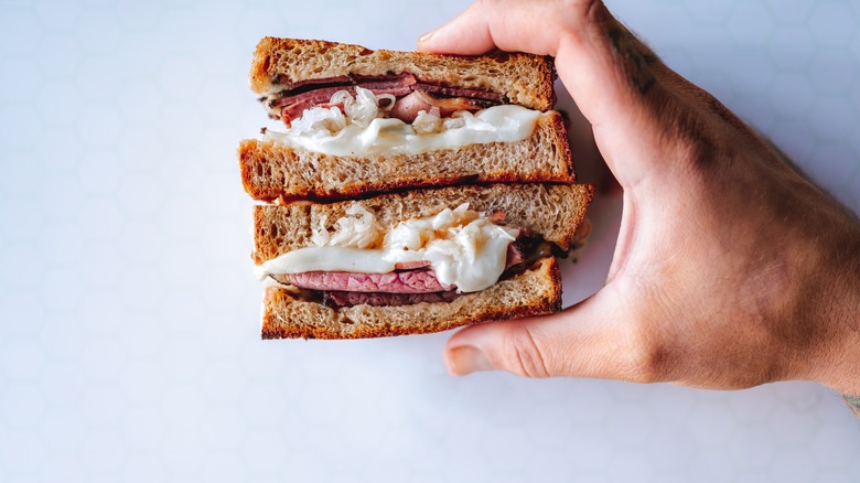 Hand holding a Reuben sandwich