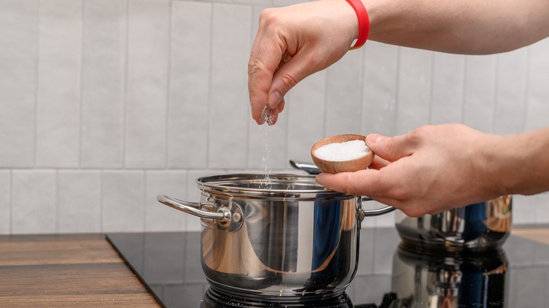 Person adding salt to pan of water