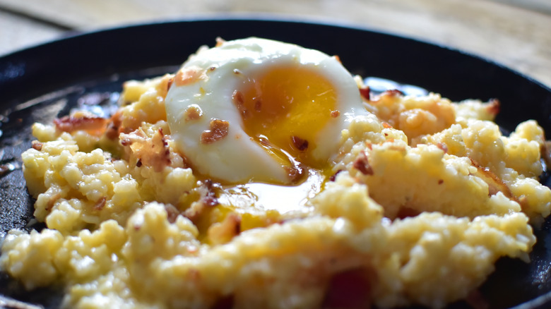 A runny egg sits on a bed of grits.