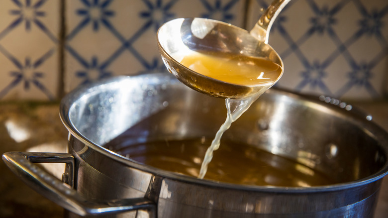 Broth in a pot is scooped up with a ladle.