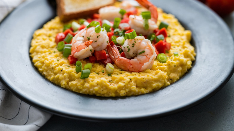 Shrimp and grits are shown in a bowl with a slice of toast on the side.