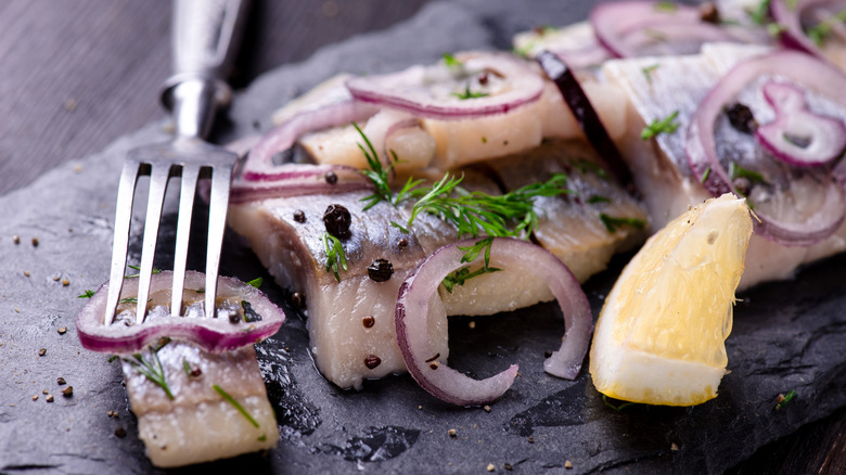 sliced herring, lemon, and onion on slate plate