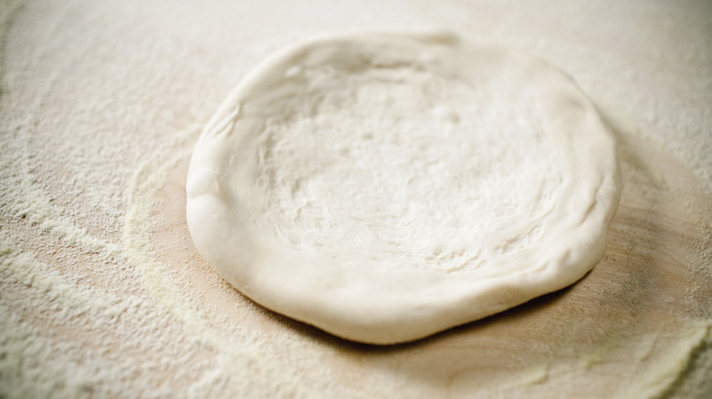 Pizza dough with flour on wooden surface