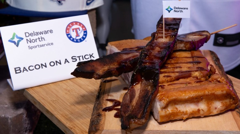 Two slices of thick-cut bacon on skewers, covered with BBQ sauce, on top of a larger piece of pork belly