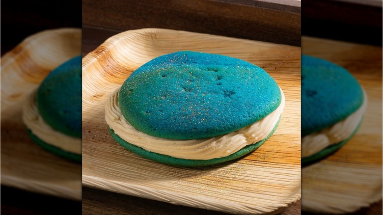 Blue whoopie pie with light beige cream in the middle on a wood tray